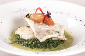 Perch fillet with spinach, sauce and tomato, decorated with eatable flowers and red leafs, placed on white plate, light background, isolated