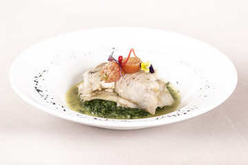 Perch fillet with spinach, sauce and tomato, decorated with eatable flowers and red leafs, placed on white plate, light background, isolated
