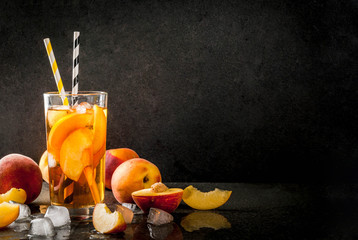 Summer refreshment drinks. Iced tea with pieces of organic home-made peach of nectarine. On a black...