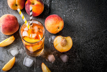 Summer refreshment drinks. Iced tea with pieces of organic home-made peach of nectarine. On a black stone background, with ice and ingredients. Copy space top view