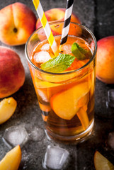 Summer refreshment drinks. Iced tea with pieces of organic home-made peach of nectarine. On a black stone background, with ice and ingredients. Copy space close view