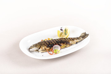 Grilled trout, served with lemon and decorated with radish and fresh leafs, light background, isolated