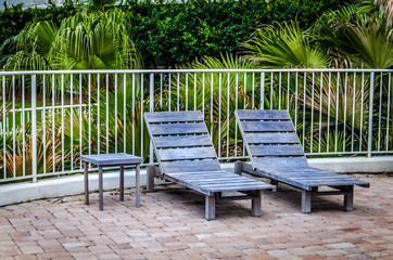 Obraz premium Rustic wooden deck chairs in tropical setting. Relax in this outdoor setting surround by tropical foliage.