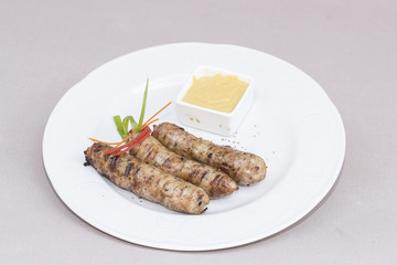 Homemade sausages, served with mustard and decorated with herbs, isolated on light background, white plate
