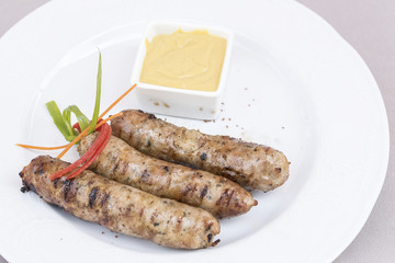 Homemade sausages, served with mustard and decorated with herbs, isolated on light background, white plate
