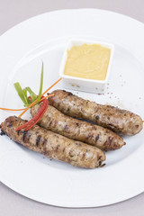 Homemade sausages, served with mustard and decorated with herbs, isolated on light background, white plate