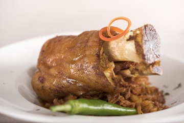 Knuckle of pork with sauerkraut and hot chili, white plate, light background, isolated