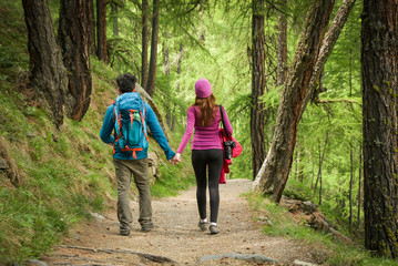 A couple hikers Hiking with backpacks walk along a beautiful mountain area holding hands . The...