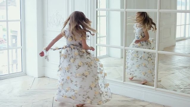 girl in long dress with flowers turns dancing in front of a large mirror