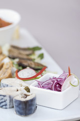 Naklejka na ściany i meble Plate with various types of fish, smoked and marinated, served with fresh salad, vegetable salad, onion salad, decorated with herbs, isolated on light background, white plate