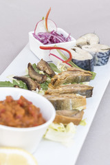 Plate with various types of fish, smoked and marinated, served with fresh salad, vegetable salad, onion salad, decorated with herbs, isolated on light background, white plate