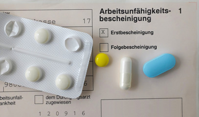 Eine vom Arzt ausgestellte Arbeitsunfähigkeitsbescheinigung mit Pillen drauf