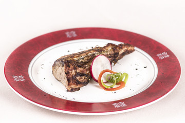 Grilled pork tenderloin, decorated with green and red leafs, placed on a white and red plate, light background