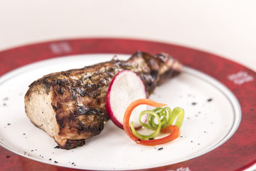 Grilled pork tenderloin, decorated with green and red leafs, placed on a white and red plate, light background