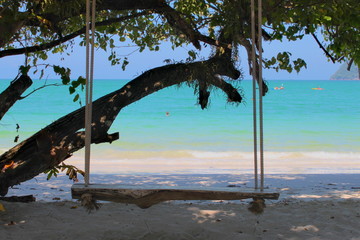 Wooden swing bench on beach under tree next to the blue sea