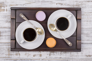 Two cups of coffee, spoon and macaron cakes on tray on white wooden table. Lifestyle concept. Top view