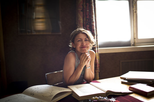 portrait of female smiling at camera while drawing inspration from books