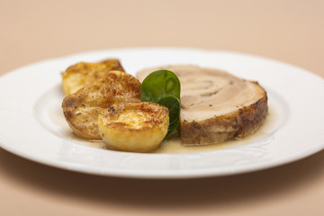 Slice roasted pork, served with potatoes and decorated with herbs, placed on white plate, light background, isolated