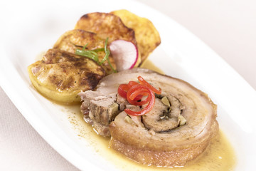 Slice roasted pork, served with potatoes and decorated with herbs, placed on white plate, light background, isolated