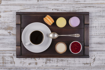 Cup of coffee, spoon and macaron cakes on tray on white wooden table. Lifestyle concept. Top view