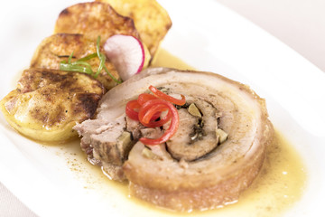 Slice roasted pork, served with potatoes and decorated with herbs, placed on white plate, light background, isolated