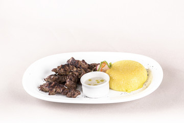 Delicious grilled pork, with polenta and garlic sauce, decorated with red and green leafs, placed on white plate, light background, isolated