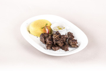 Delicious grilled pork, with polenta and garlic sauce, decorated with red and green leafs, placed on white plate, light background, isolated