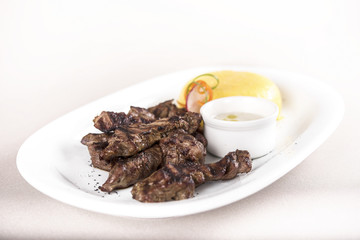 Delicious grilled pork, with polenta and garlic sauce, decorated with red and green leafs, placed on white plate, light background, isolated
