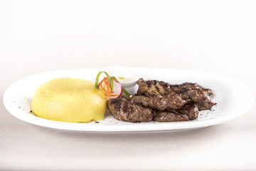Delicious grilled pork, with polenta and garlic sauce, decorated with red and green leafs, placed on white plate, light background, isolated