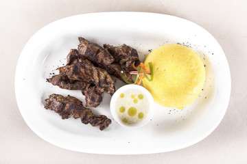 Delicious grilled pork, with polenta and garlic sauce, decorated with red and green leafs, placed on white plate, light background, isolated