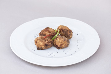 Fried pane sweetbreads, decorated with herbs, isolated on light background, white plate