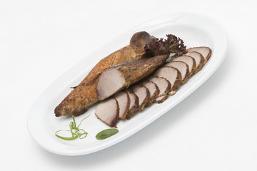 Pork tenderloin, decorated with green and red leafs, placed on a white and red plate, light background