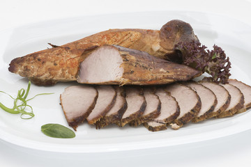 Pork tenderloin, decorated with green and red leafs, placed on a white and red plate, light background