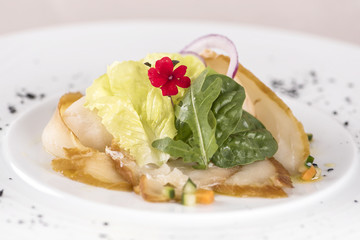 Fresh appetizer with smoked white fish, rucola, baby spinach and green salad, with red eatable flowers, placed on white plate, light background, isolated