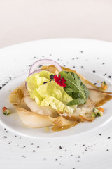 Fresh appetizer with smoked white fish, rucola, baby spinach and green salad, with red eatable flowers, placed on white plate, light background, isolated