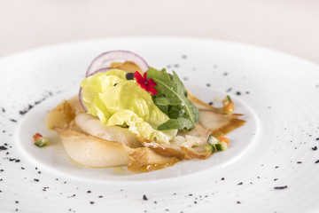 Fresh appetizer with smoked white fish, rucola, baby spinach and green salad, with red eatable flowers, placed on white plate, light background, isolated