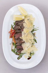 Fresh appetizer with prosciutto ham and slices of parmesan, decorated with green leaf, placed on white plate, light background, isolated