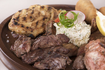Traditional Romanian food plateau, with sausages, grilled meat, sweetbreads, potatoes, pickles, mustard, polenta, mushrooms, mici and vegetable salad, decorated with herbs, isolated on light backgroun