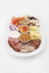 Traditional Romanian food plateau, containing different types of meat and cheese, tomatoes, onion, cucumber, olives and salads: “zacusca”, eggplant salad and beans salad, decorated with herbs, isolate