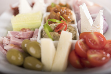 Traditional Romanian food plateau, containing different types of meat and cheese, tomatoes, onion, cucumber, olives and salads: “zacusca”, eggplant salad and beans salad, decorated with herbs, isolate