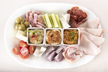 Traditional Romanian food plateau, containing different types of meat and cheese, tomatoes, onion, cucumber, olives and salads: “zacusca”, eggplant salad and beans salad, decorated with herbs, isolate