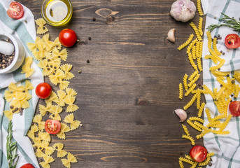 Ingredients for making homemade vegetarian pasta, olive oil, herbs, cherry tomatoes lined border on napkins, on rustic wooden background, with space for text