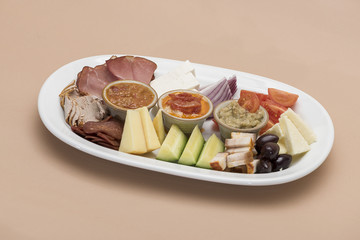 Traditional Romanian food plateau, containing different types of meat and cheese, tomatoes, onion, cucumber, olives and salads: “zacusca”, eggplant salad and beans salad, decorated with herbs, isolate