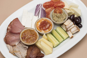 Traditional Romanian food plateau, containing different types of meat and cheese, tomatoes, onion, cucumber, olives and salads: “zacusca”, eggplant salad and beans salad, decorated with herbs, isolate