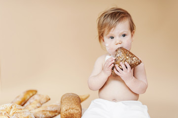 Fresh pastries in a bakery. The child eats a roll with appetite. The little girl with a fair hair bites bread.