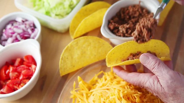Older man prepares a taco with tomatoes, onions, lettuce, ground beef and grated cheese