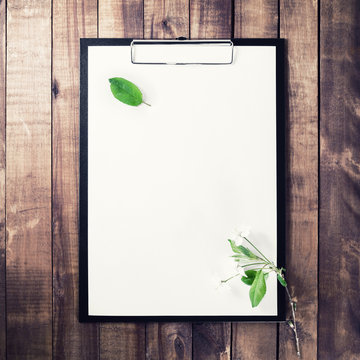 Photo of clipboard with blank letterhead, cherry blossoms with green leaves on vintage wooden background. Template for placing your design. Top view.