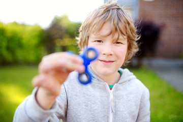 Cute school boy playing with fidget spinner on the playground. Popular stress-relieving toy for school kids and adults.