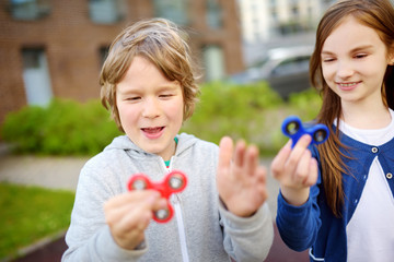 Two funny friends playing with fidget spinners on the playground. Popular stress-relieving toy for school kids and adults.