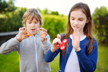 Two funny friends playing with fidget spinners on the playground. Popular stress-relieving toy for...